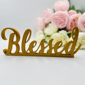 May include: Gold-coloured wooden sign with the word "Blessed" in a cursive font.