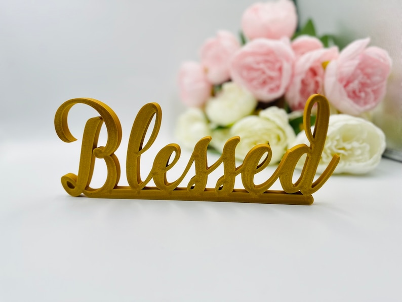 May include: Gold-coloured wooden sign with the word "Blessed" in a cursive font.
