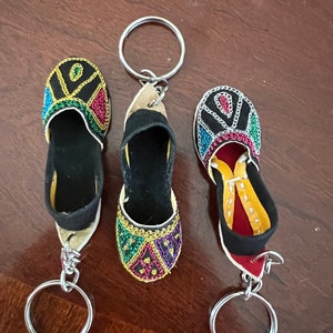 Pode incluir: Tr&ecirc;s chaveiros em forma de sapato bordados com cores vibrantes com argolas de prata. Os sapatos s&atilde;o pretos com bordados coloridos e est&atilde;o presos a argolas de prata.