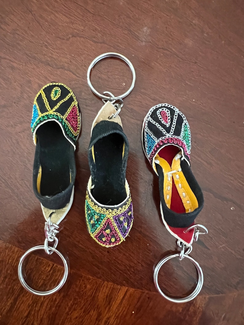 Pode incluir: Tr&ecirc;s chaveiros em forma de sapato bordados com cores vibrantes com argolas de prata. Os sapatos s&atilde;o pretos com bordados coloridos e est&atilde;o presos a argolas de prata.
