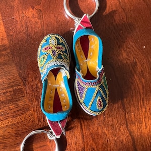 Pode incluir: Um par de chaveiros de pantuflas bordadas em azul e dourado com detalhes vermelhos. Os pingentes s&atilde;o presos a um chaveiro prateado.