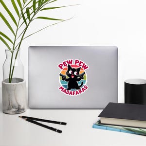May include: A black cat with big eyes holds two guns and is surrounded by a rainbow coloured circle with the text "PEW PEW MADAFAKAS".