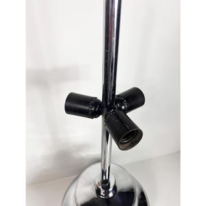 Op de afbeelding: Een chromen vloerlamp met drie zwarte lampfittingen. De lamp heeft een ronde voet en een enkele paal.