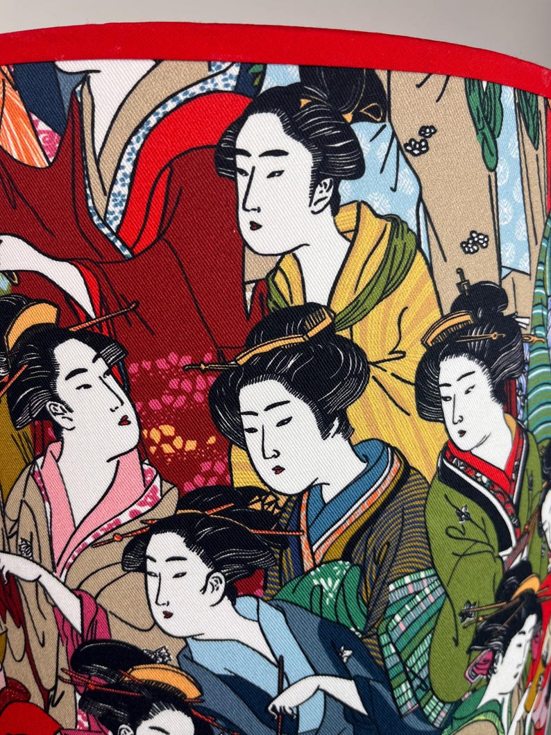 Op de afbeelding: Een kleurrijke stof met een herhalend patroon van Japanse vrouwen in traditionele kleding. De stof heeft een verscheidenheid aan kleuren, waaronder rood, groen, blauw, geel en wit.