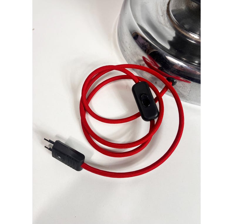 Op de afbeelding: Een rood elektrisch snoer met een zwarte in-line schakelaar en een zwarte stekker. Het snoer is opgerold en de stekker is zichtbaar.