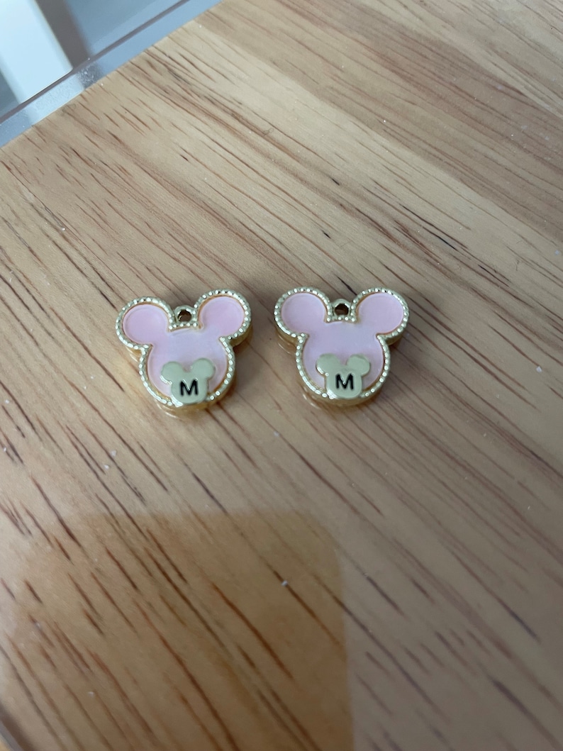 May include: Two pink and gold mouse-shaped charms with the letter "M" on each.