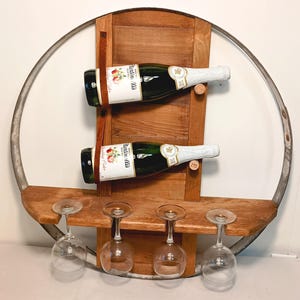Peut inclure: Un porte-bouteilles en bois rustique, fabriqué à partir d'un tonneau recyclé, avec un cerceau métallique circulaire. Il contient deux bouteilles de vin maintenues par des lanières de cuir et une étagère pour quatre verres à vin.