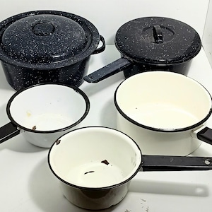May include: A collection of vintage enamelware pots and pans. The set includes two pots with lids, and three saucepans. The cookware features a speckled black and white design with black handles and rims. The interior of the pots and pans are white.