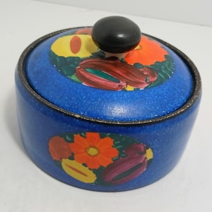 Könnte beinhalten: Ein blauer Keramiktopf mit Deckel und schwarzem Knauf. Der Topf ist mit bunten Obst- und Blumenmotiven verziert. Der Rand des Topfes und des Deckels ist schwarz umrandet.