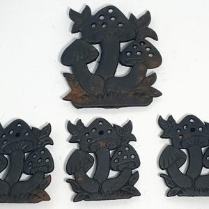 May include: Five dark brown mushroom-shaped decorations. Each mushroom has a cap with small holes and is attached to a base with leaves. The items are arranged on a white surface.