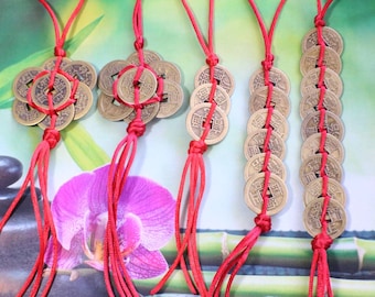 May include: Five sets of Chinese lucky coins strung on red cords with tassels. The coins are brass colored and have Chinese characters on them.