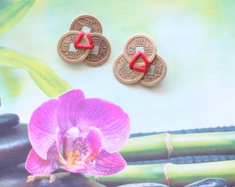 May include: Two sets of bronze-colored Chinese coins, each set with three coins held together by a red triangle. The background features a pink orchid, black stones, and bamboo stalks, creating a zen-like aesthetic.