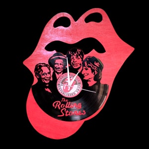 Könnte beinhalten: Eine rote, zungenförmige Uhr aus Holz mit einem schwarzen Vinyl-Zifferblatt. Die Uhr zeigt ein Schwarzweißbild der Rolling Stones-Bandmitglieder und den Text "The Rolling Stones Established 1962".