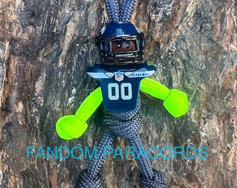May include: A green, black, and blue paracord keychain with a football player figure. The figure is wearing a helmet, jersey, and pants. The jersey has the number "00" and the text "NFL" and "SEAHWAKS".