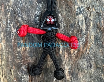 May include: Black and red paracord keychain with a Spiderman head charm. The keychain is tied in a figure shape with red arms and black legs.