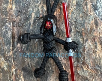 May include: Black paracord keychain with a red lightsaber and a Darth Maul Lego minifigure head. The keychain is in the shape of a person with arms outstretched.