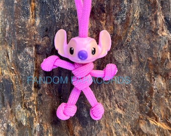 May include: Pink Stitch character keychain made from pink paracord with a purple nose. The keychain is hanging from a wooden surface.