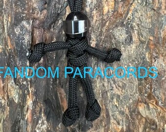 May include: Black paracord keychain with a black helmet charm. The keychain is in the shape of a stick figure.