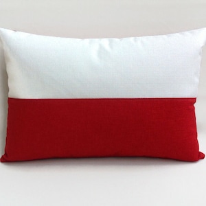 Puede incluir: Una almohada blanca y roja con un diseño de rayas horizontales. La almohada está hecha de una tela suave y texturizada.