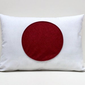 Puede incluir: Almohada blanca con un círculo rojo grande en el centro. El círculo es de una tela diferente a la de la almohada.