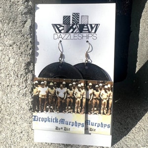 May include: Black circular earrings with a Dropkick Murphys album cover image featuring a group of men in workwear. The album cover text reads "Dropkick Murphys Do or Die".