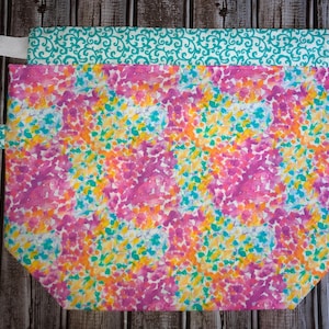 May include: A reusable shopping bag with a colorful floral print and a teal and white patterned trim. The bag has white drawstrings and a small tag that says "Handmade with Love".