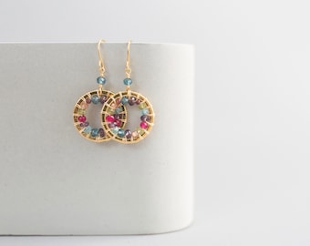 May include: Gold hoop earrings with a wire wrapped design featuring a variety of colorful gemstones, including pink, red, blue, and green.
