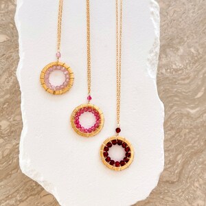 May include: Three gold necklaces with circular pendants featuring different colored gemstones. The pendants are made of wire wrapped around a circle of small gemstones. The necklaces are on a white background.