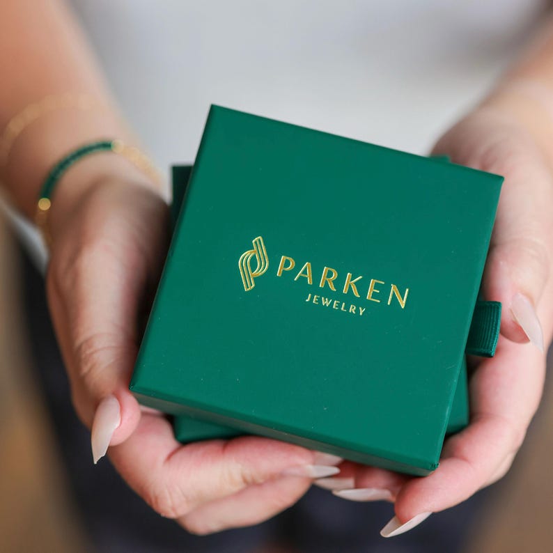 K&ouml;nnte beinhalten: Eine gr&uuml;ne Schmuckschatulle mit einem goldenen Logo, auf dem "Parken Jewelry" steht.