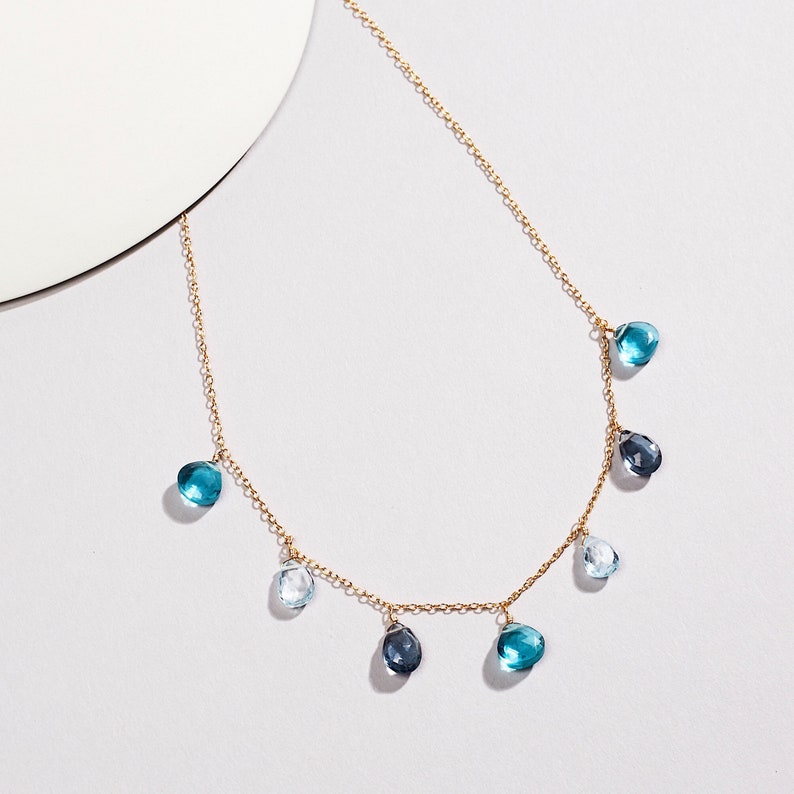 K&ouml;nnte beinhalten: Eine goldene Kettenkette mit tropfenf&ouml;rmigen blauen, hellblauen und klaren Edelsteinen, die daran h&auml;ngen.