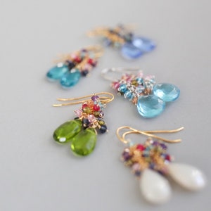 May include: Five pairs of dangle earrings with colorful gemstone beads and teardrop-shaped stones. The stones are in shades of blue, green, and white.
