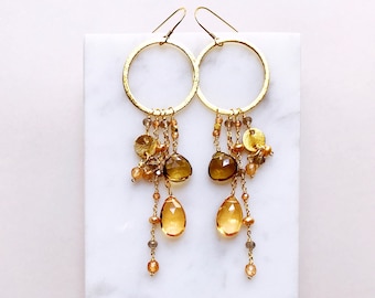 May include: Gold hoop earrings with a dangling chain of gold beads, brown and gold stones, and gold discs.