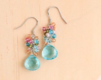 May include: A pair of silver dangle earrings with a teardrop shaped blue gemstone and a cluster of colorful beads.