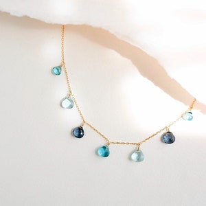 K&ouml;nnte beinhalten: Eine goldene Kettenkette mit tropfenf&ouml;rmigen blauen Edelsteinen, die daran h&auml;ngen. Die Kette liegt auf einem wei&szlig;en Hintergrund.