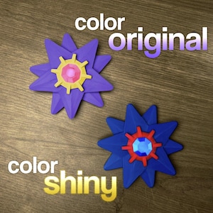 Two star-shaped objects with a flower-like design. The original is purple with yellow and pink accents. The shiny version is blue with red and blue accents. The words 'color original' and 'color shiny' are written above and below the objects.