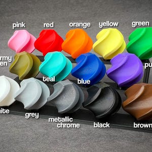 May include: A collection of twelve colorful, abstract, spiral-shaped objects. Colors include pink, red, orange, yellow, green, army green, teal, blue, purple, white, grey, metallic chrome, black, and brown. Each object is labeled with its respective color.