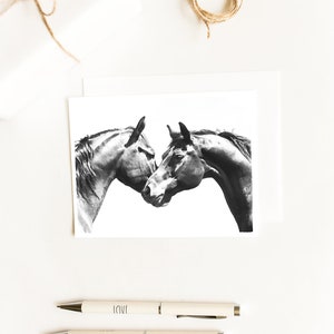 May include: Black and white illustration of two horses' heads nuzzling each other on a white card. The card is on a white surface with two white pens with the words "LOVE" and "HOPE" printed on them.