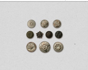 May include: Nine antique metal brads with various designs, including a star, a heart, and a floral pattern. The brads are arranged in a grid pattern on a light gray background. The text "Antique Brads Vol. 1" is visible at the top of the image.