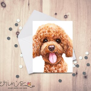 May include: A watercolor greeting card featuring a brown poodle with a pink tongue sticking out. The card is inside a white envelope, with decorative confetti scattered around on a wooden surface. The card is a portrait of a dog.