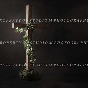May include: A wooden cross with a dark brown finish, adorned with white flowers and green foliage. The cross is set against a dark background. The text "PROPERTY OF STUDIO M PHOTOGRAPHY" is visible.