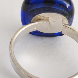May include: A silver ring featuring a smooth, rounded, deep blue glass cabochon set in a polished metal band. The interior of the band is clearly stamped with the number 925, indicating the silver content of this piece of jewelry.