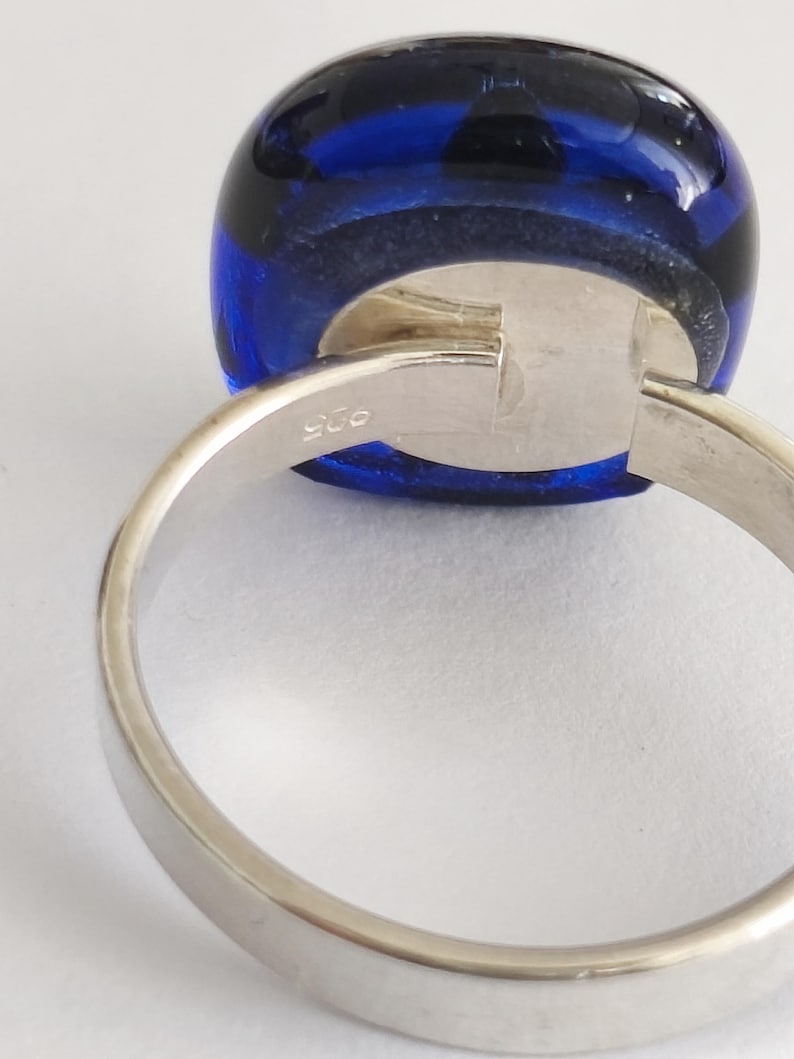 May include: A silver ring featuring a smooth, rounded, deep blue glass cabochon set in a polished metal band. The interior of the band is clearly stamped with the number 925, indicating the silver content of this piece of jewelry.