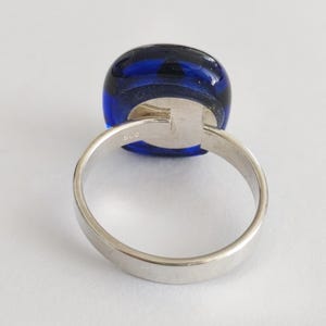 May include: A silver ring featuring a smooth, rounded, deep blue glass cabochon set in a polished metal band. The interior of the band is clearly stamped with the hallmark 925, indicating sterling silver composition for this jewelry piece.