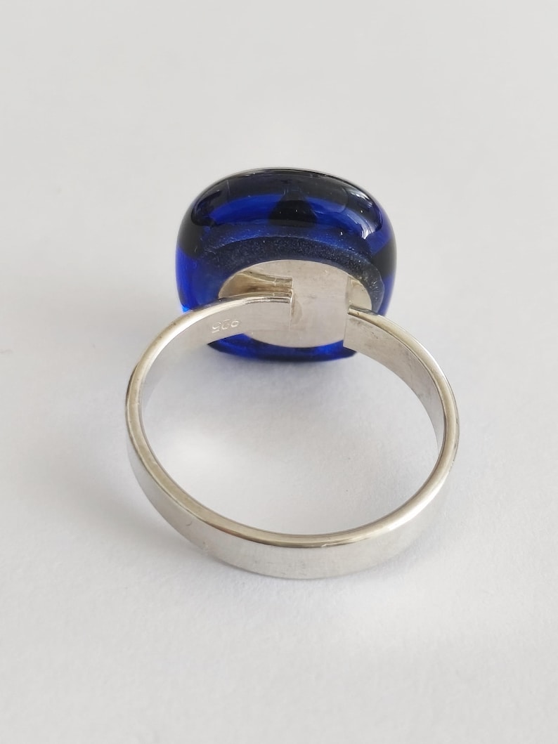 May include: A silver ring featuring a smooth, rounded, deep blue glass cabochon set in a polished metal band. The interior of the band is clearly stamped with the hallmark 925, indicating sterling silver composition for this jewelry piece.