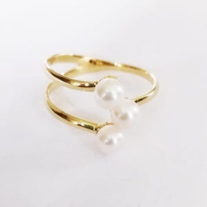 Peut inclure: Une bague en or avec trois perles blanches. La bague est à double bande et les perles sont regroupées.