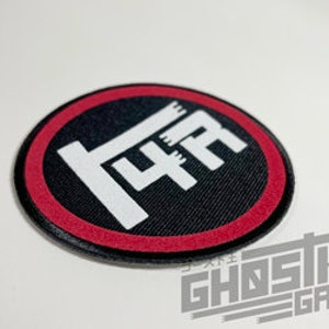 May include: A red and black circular patch with a white graphic of the Japanese word "IYA" in a stylized font.