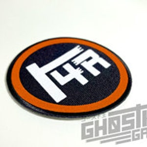 May include: A black and white embroidered patch with the text "144" in a white circle with an orange outline.