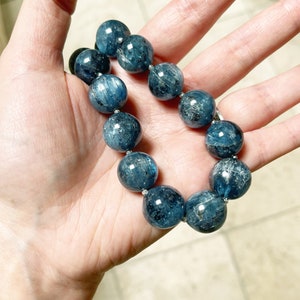 K&ouml;nnte beinhalten: Ein blaues Edelstein-Armband mit runden Perlen. Das Armband besteht aus nat&uuml;rlichen Steinen und ist auf einer silbernen Kette aufgef&auml;delt.