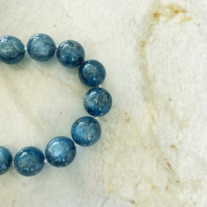 K&ouml;nnte beinhalten: Ein blaues Edelstein-Armband mit runden Perlen. Das Armband besteht aus nat&uuml;rlichen Steinen und ist auf einem Silberdraht aufgef&auml;delt.