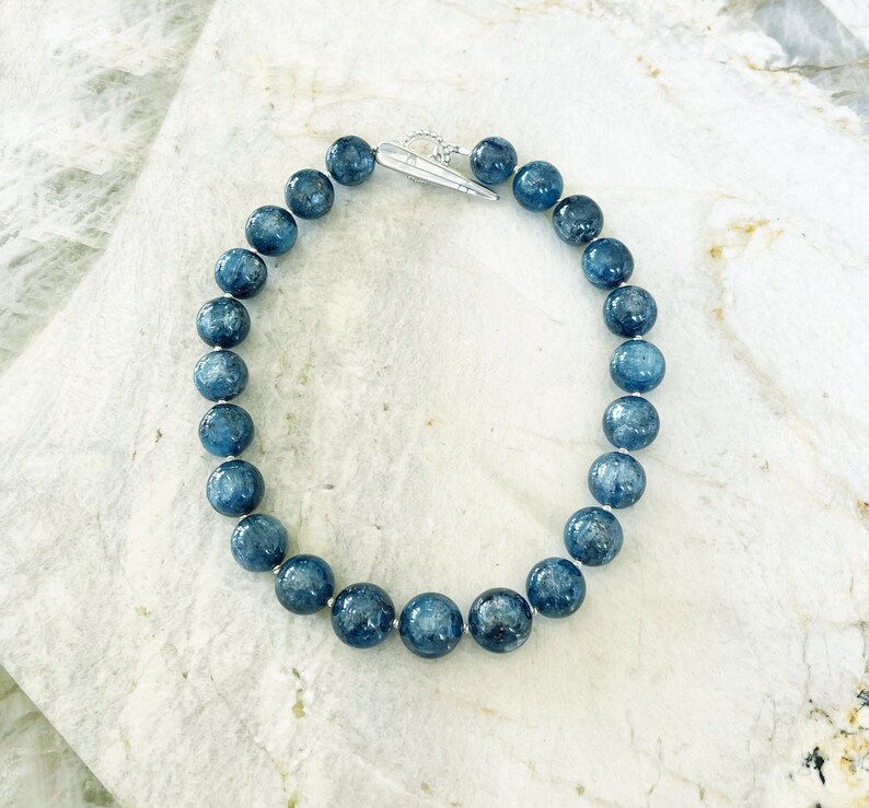 K&ouml;nnte beinhalten: Eine Halskette aus blauen Edelsteinen mit einem silbernen Verschluss. Die Halskette besteht aus runden Perlen und ist etwa 45 cm lang.